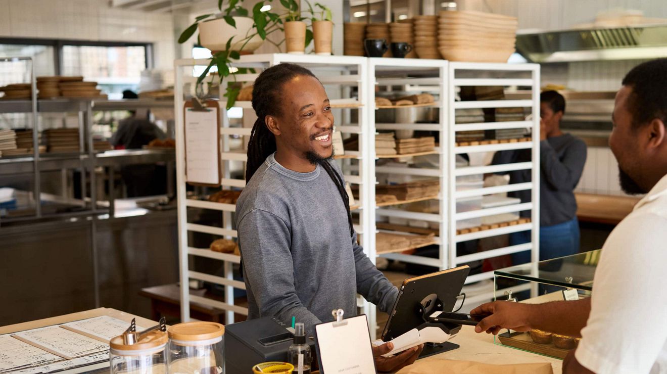 Un empleado atiende a un cliente en una panadería artesanal utilizando una tablet como POS.