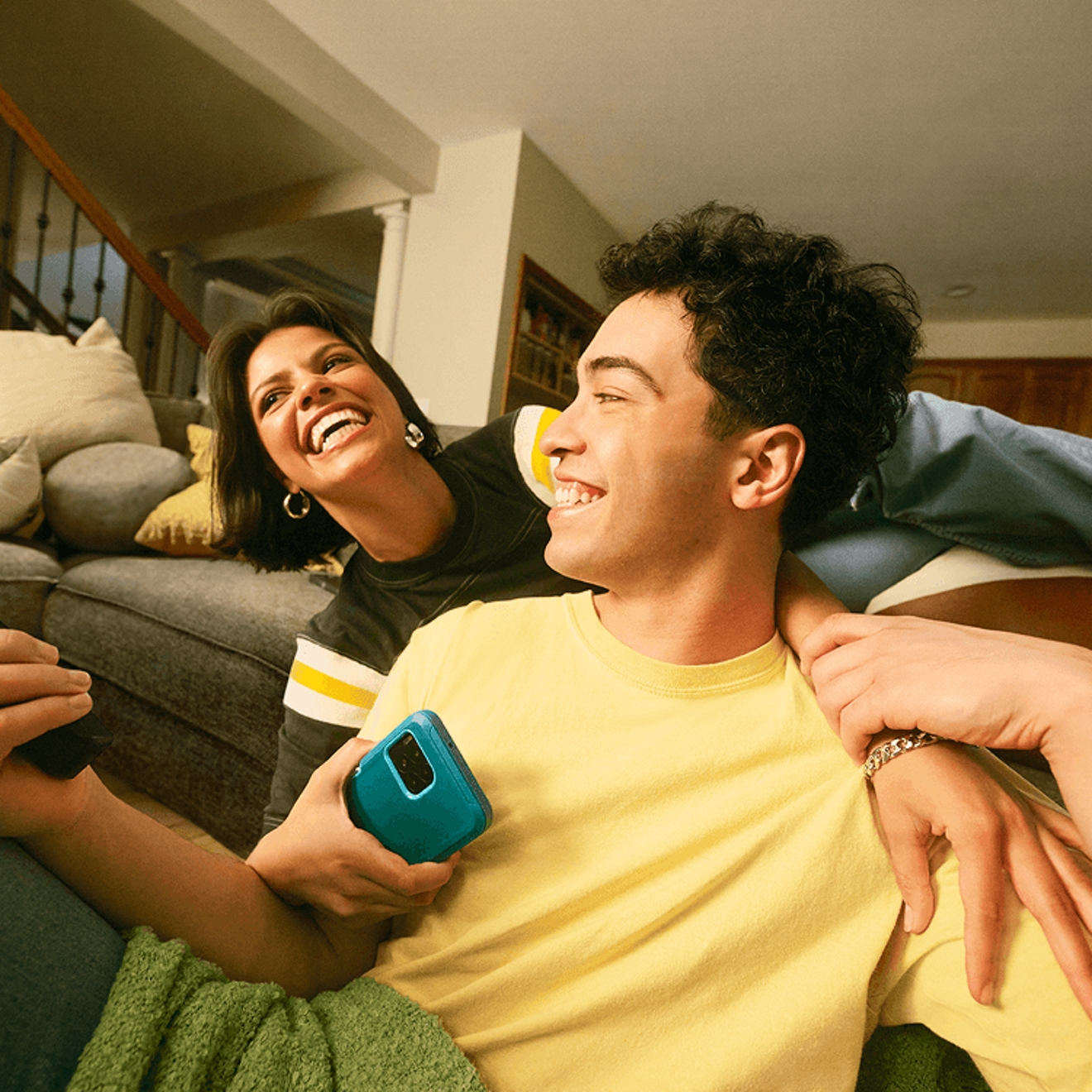 ​​Una pareja joven se ríe frente al televisor, sosteniendo sus smartphones.​