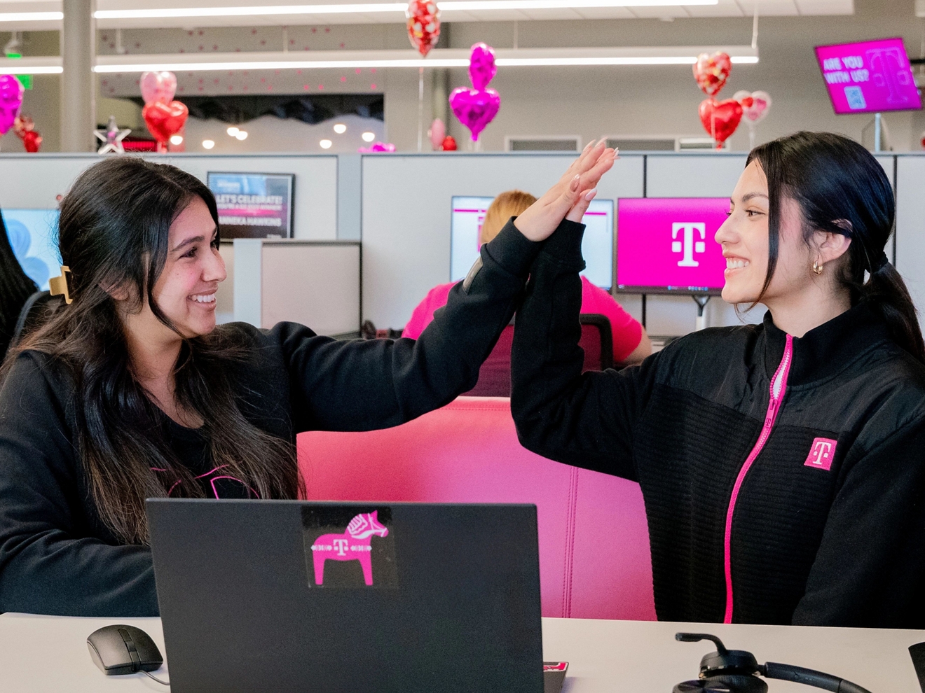 ​​Dos colegas de T-Mobile chocan los cinco sentadas en sus escritorios.​