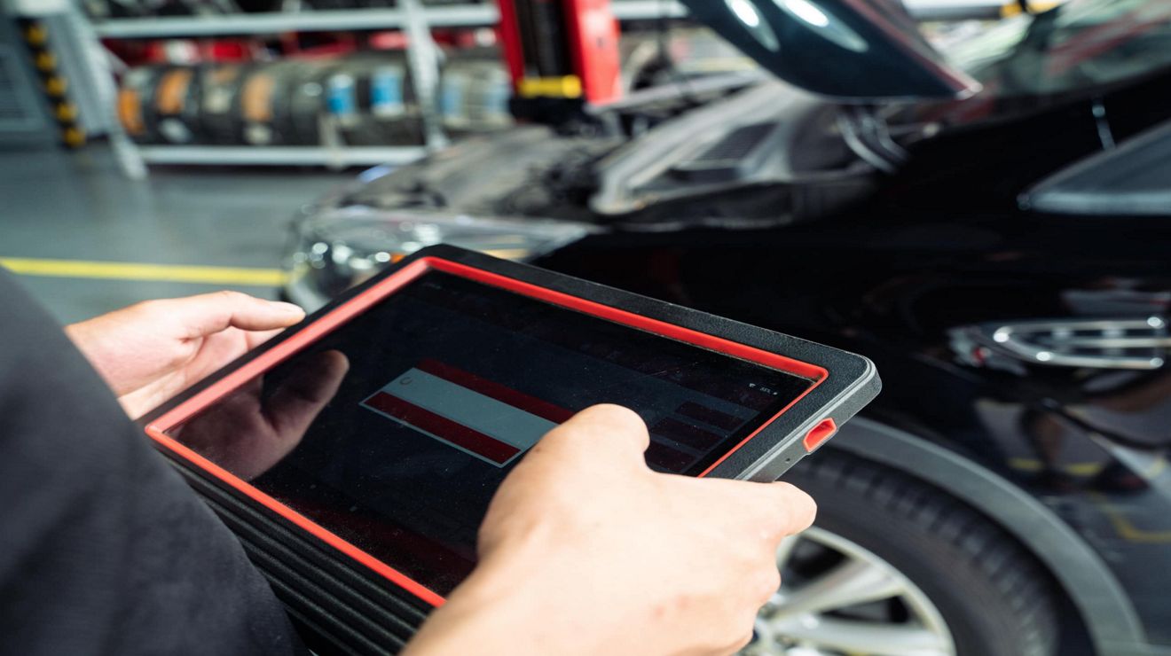 An auto repair specialist inspects a vehicle and works with a connected tablet.