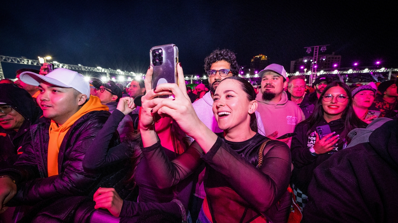 Una multitud de asistentes al concierto sonríe y toma fotos con sus teléfonos.