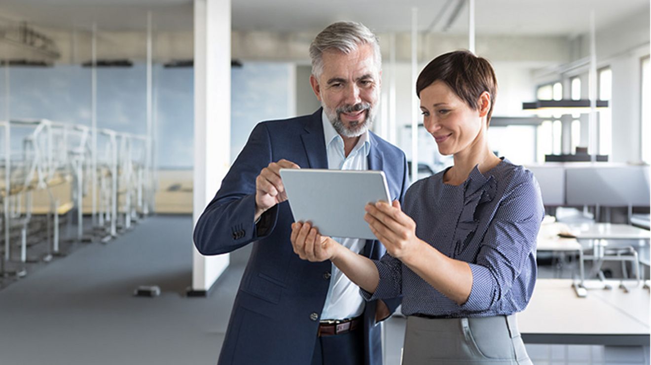 Two business owners review metrics on a tablet in an empty open office space.