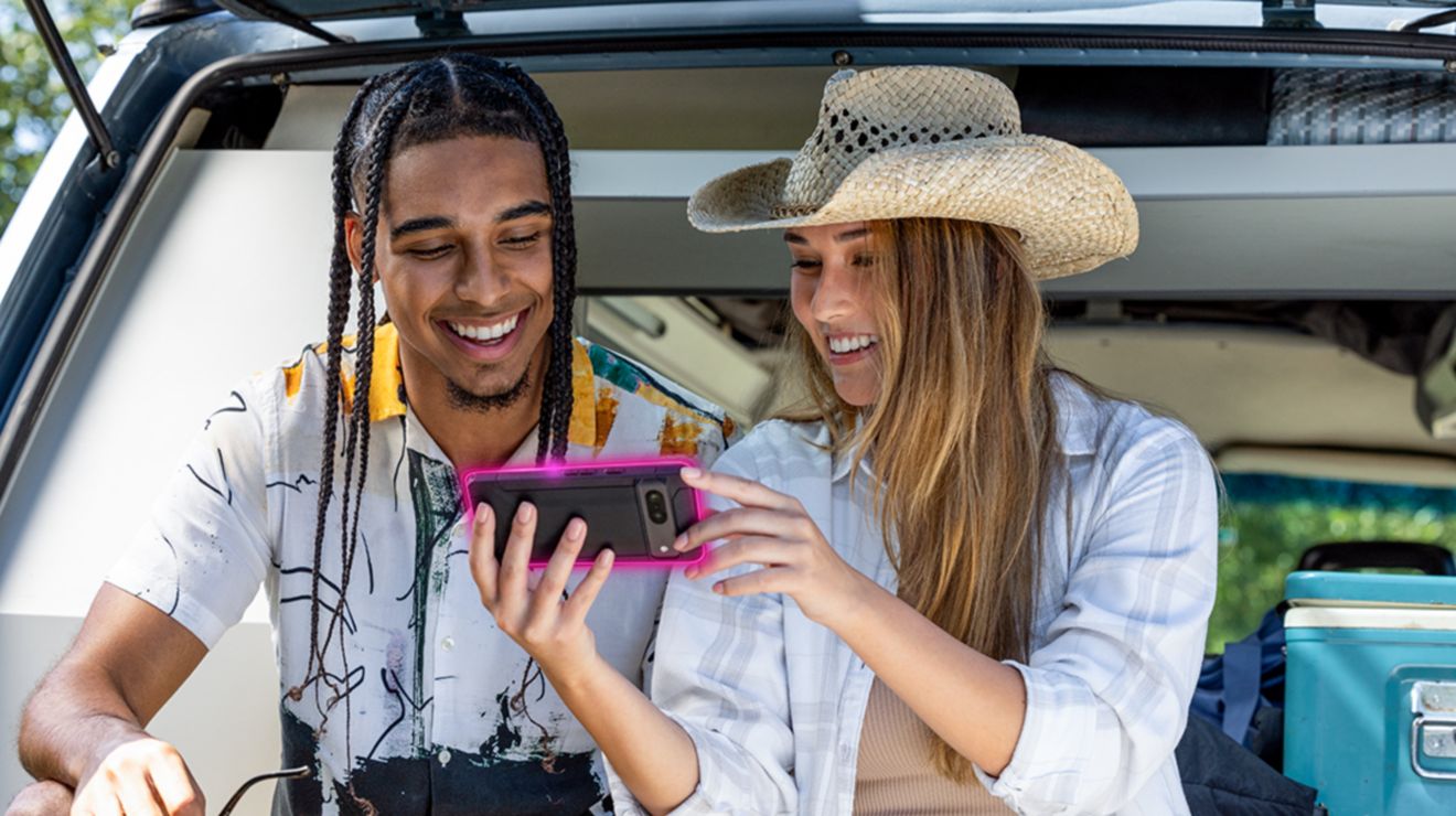 ​Una mujer con sombrero vaquero y un hombre sonriente miran juntos la pantalla de un teléfono.