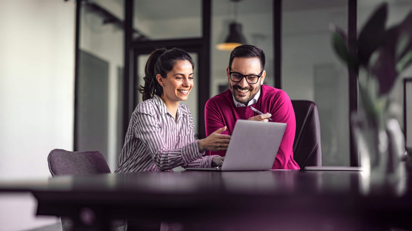 Dos compañeros de trabajo comparten una laptop y revisan un proyecto juntos.