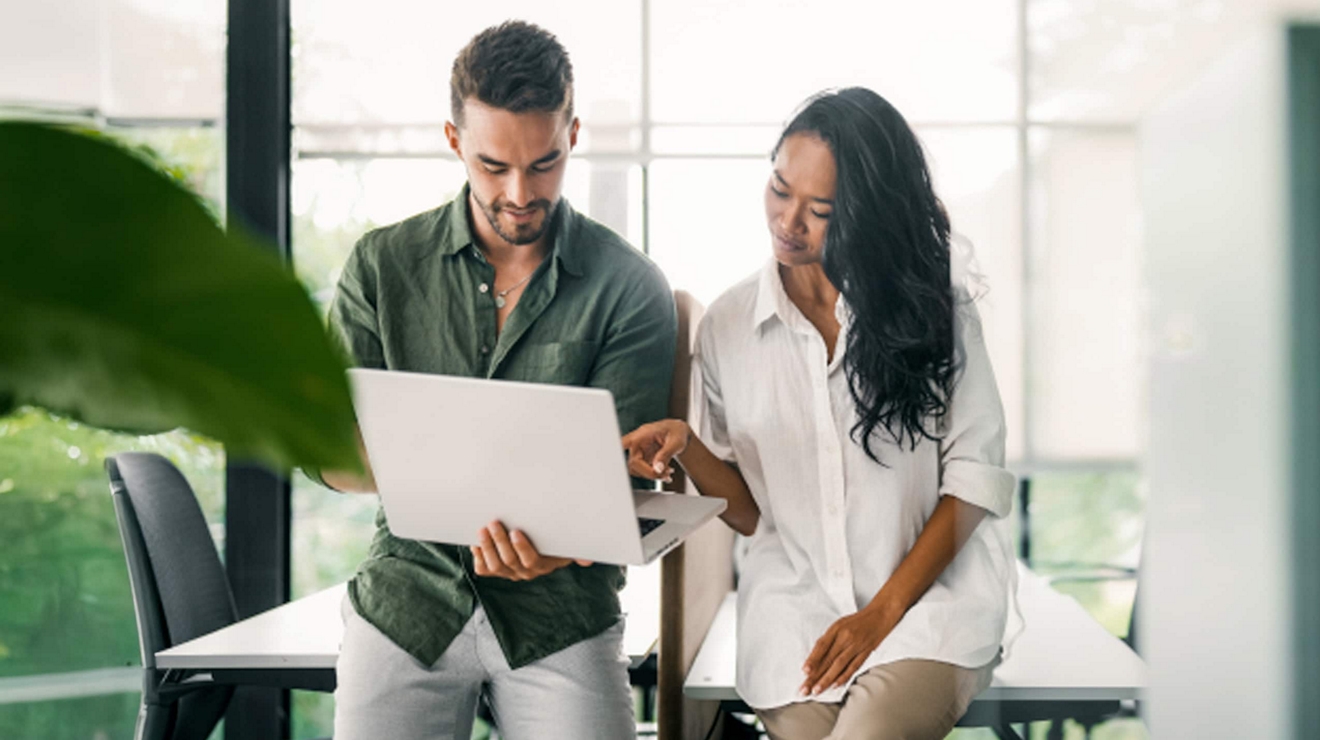 Dos colegas revisan información en una laptop antes de una reunión en una sala de conferencias.
