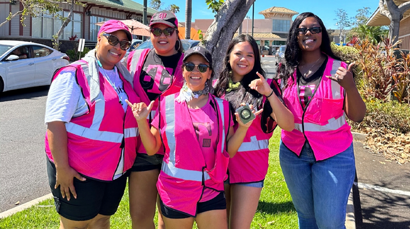 Un grupo de voluntarios con chalecos magenta sonríe mientras posan juntos al aire libre.