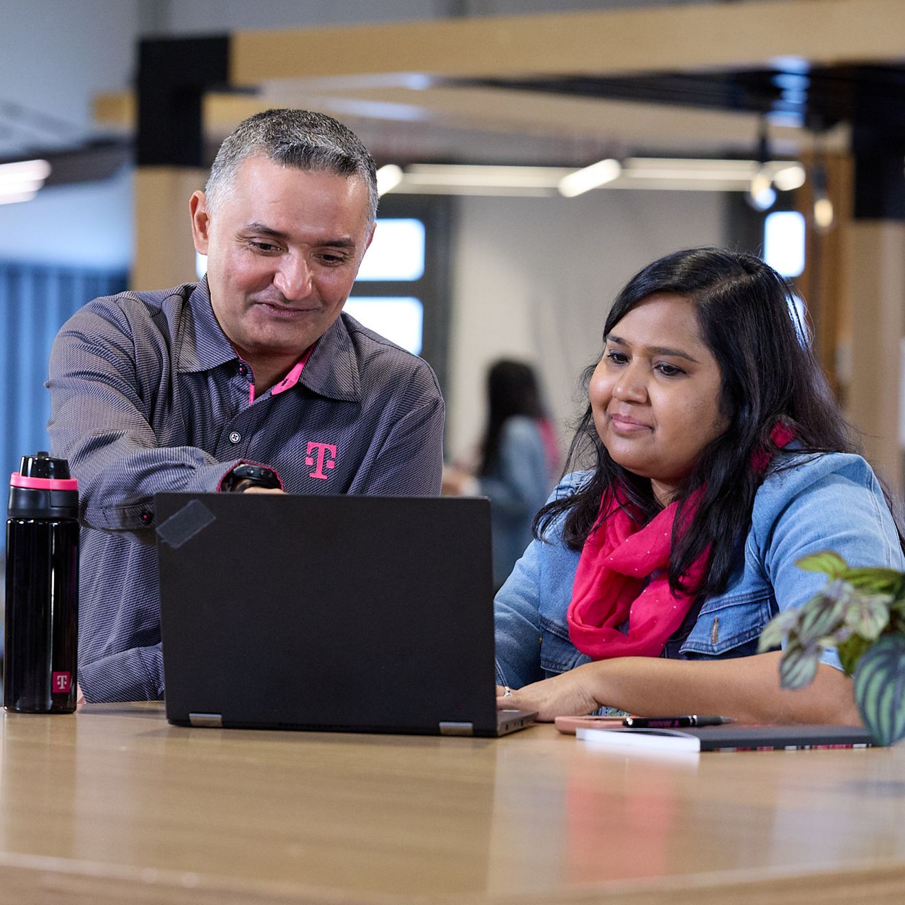 ​​​​​​​Dos empleados de T-Mobile están sentados juntos, sonriendo mientras miran la pantalla de una laptop.