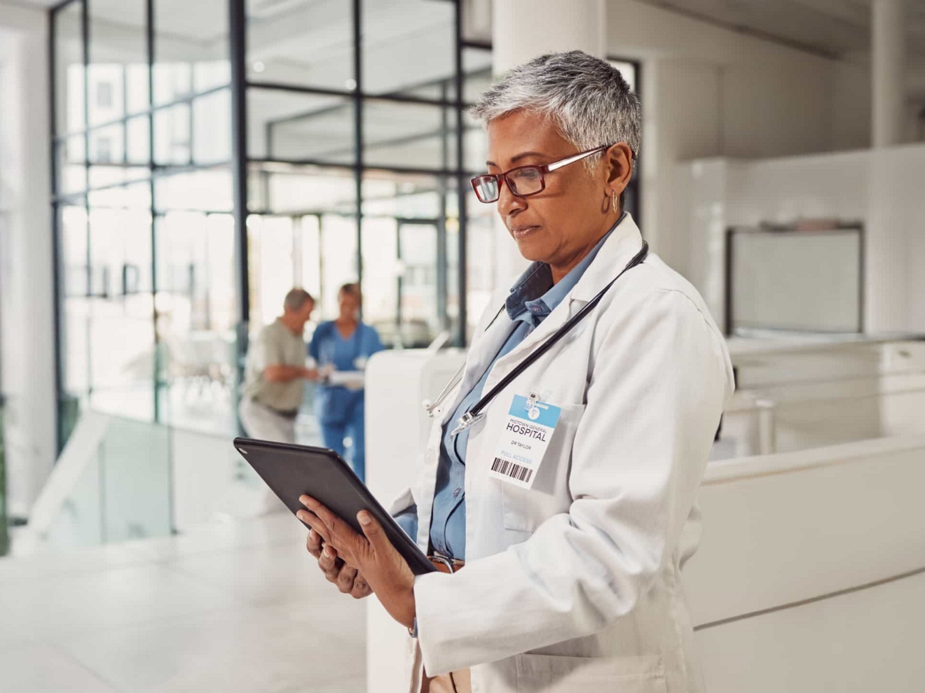 Un médico en el pasillo de un hospital estudia información en la pantalla de su tablet.