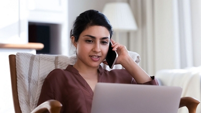 Mujer hablando por teléfono y usando su laptop en su casa.