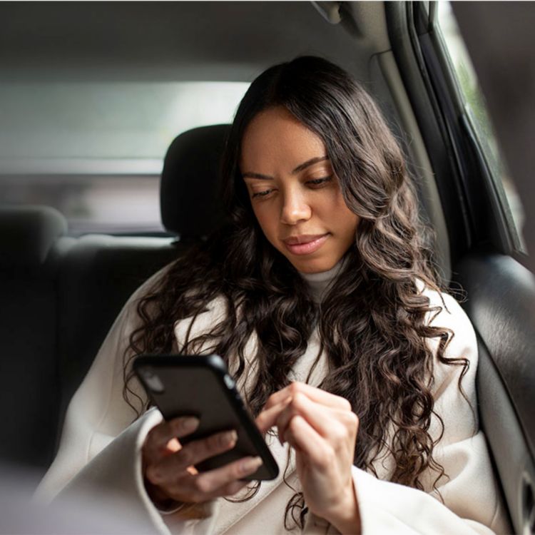 Mujer joven explorando contenido en su teléfono mientras viaja en el asiento trasero de un auto.