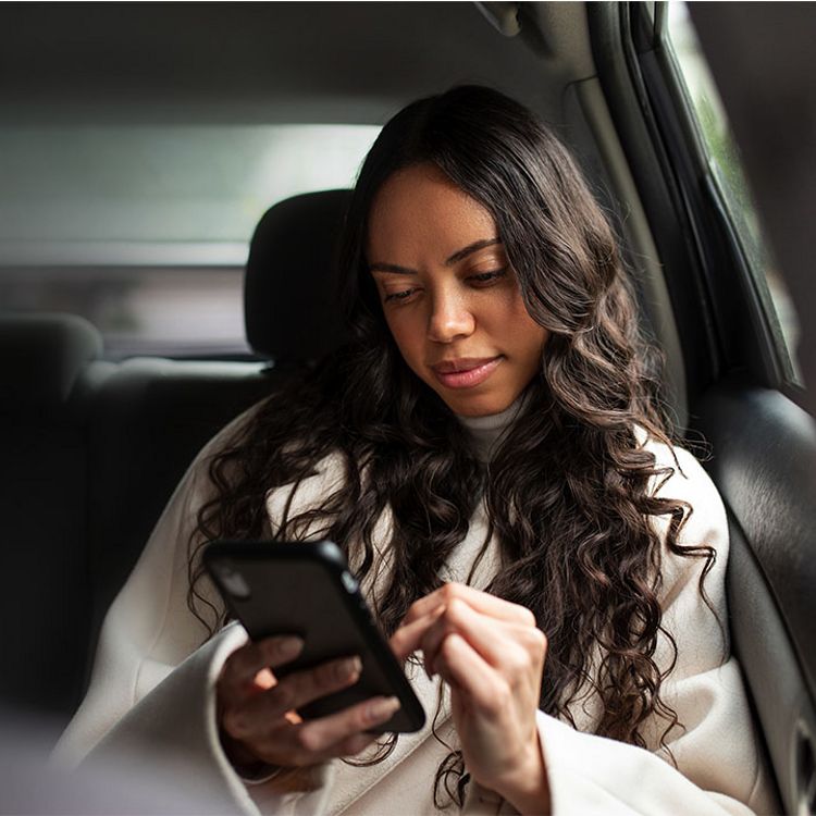 Mujer joven explorando contenido en su teléfono mientras viaja en el asiento trasero de un auto.