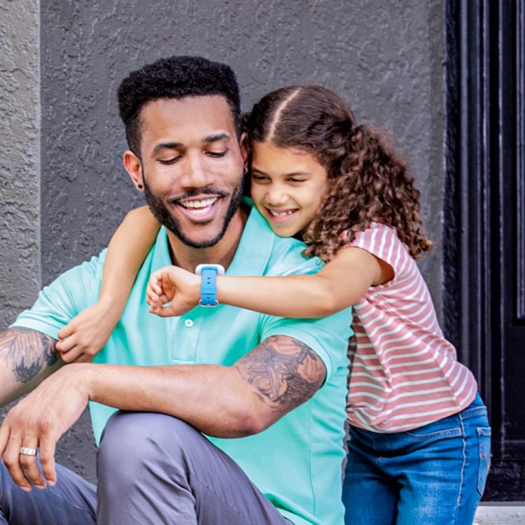 Girl wraps arms around her dad’s neck and shows off her SyncUP kid’s watch.
