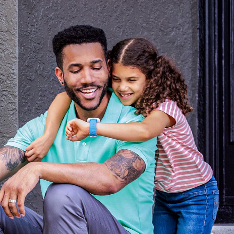 Niña con los brazos alrededor del cuello de su papá mostrando su reloj SyncUP kids.
