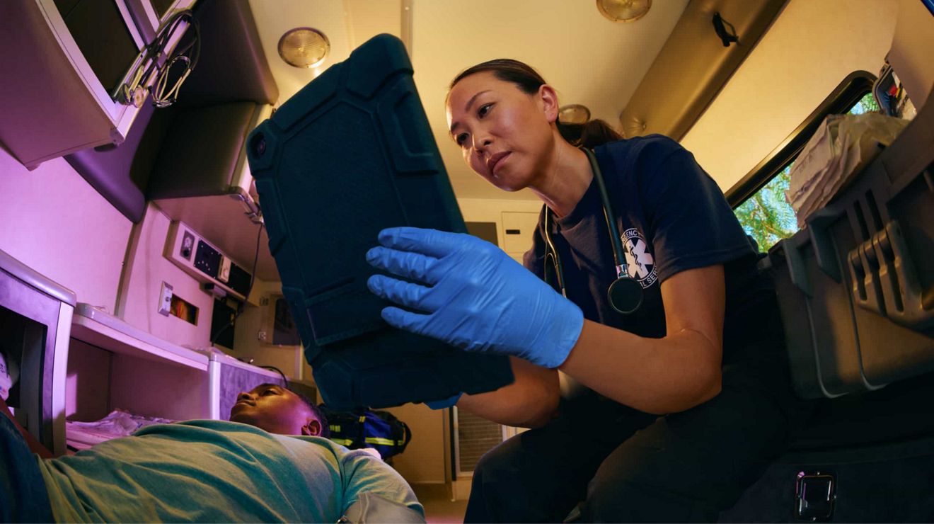 Una miembro de servicios de emergencia usa una tablet para coordinar la atención de un paciente en el interior de una ambulancia.