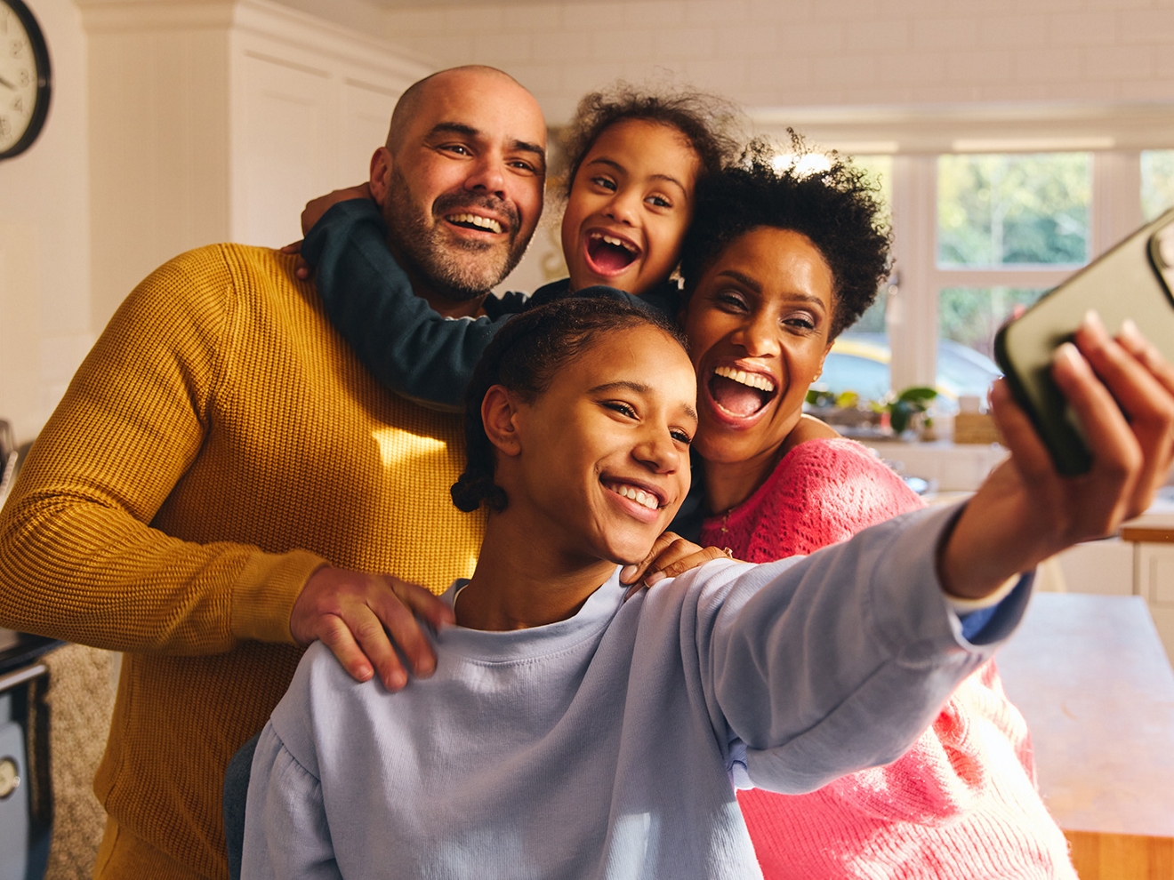 Una sonriente familia de cuatro se agrupa para hacer un selfie en su casa.