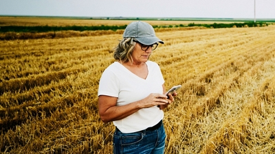Un agricultor rural se encuentra en un campo de trigo y envía un mensaje desde su smartphone.