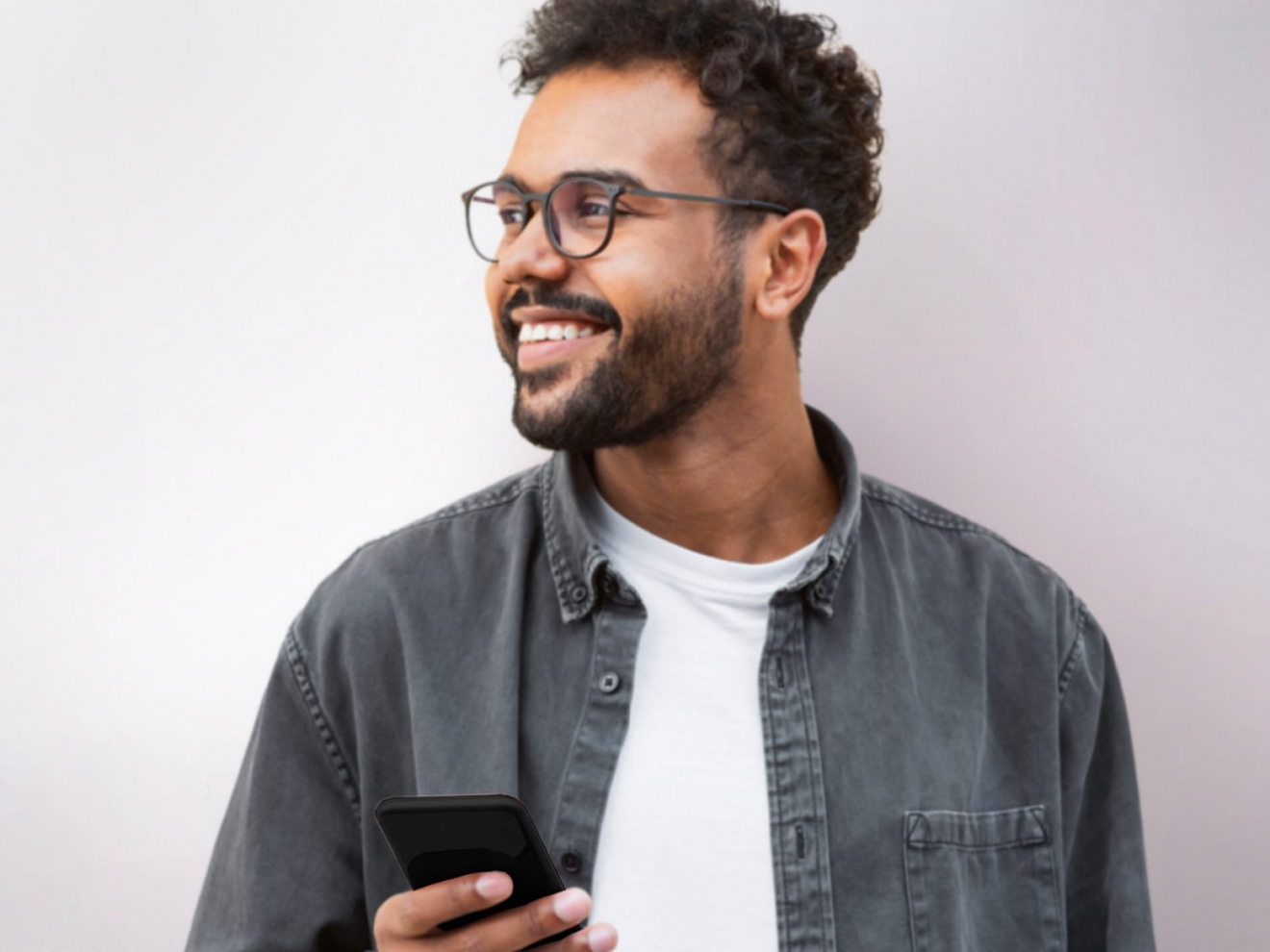 Persona mirando a lo lejos con una sonrisa en el rostro y un smartphone en la mano.