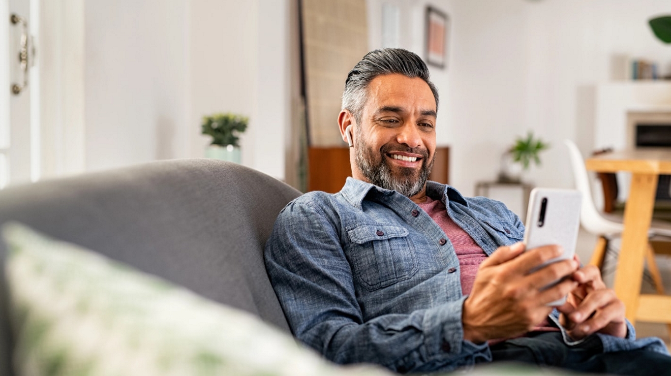 Persona relajada en un sofá, escuchando música desde su smartphone con audífonos.