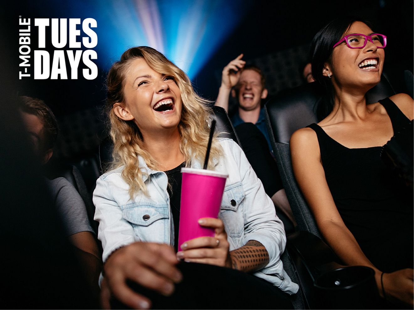 Dos mujeres sentadas una al lado de la otra en un cine, riendo.