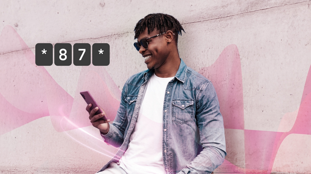 Un hombre con camiseta blanca, chaqueta de mezclilla y gafas de sol sonríe mientras usa su teléfono.