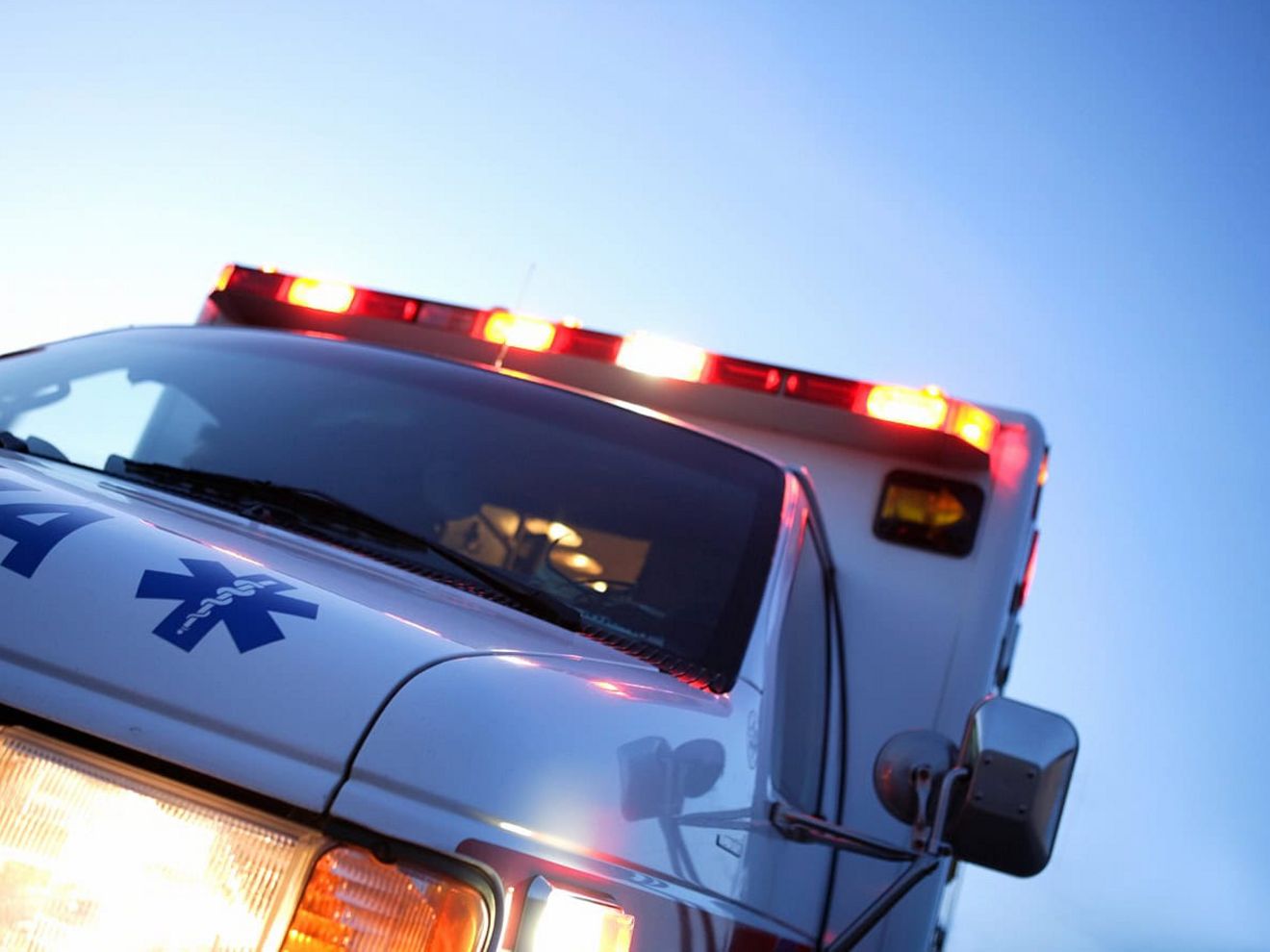 La parte delantera de una ambulancia con los faros y las luces intermitentes del techo encendidos.