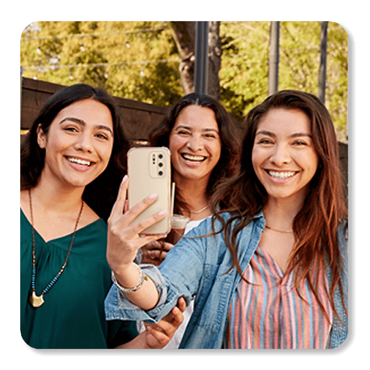 Tres mujeres sonríen tomándose un selfie en un parque