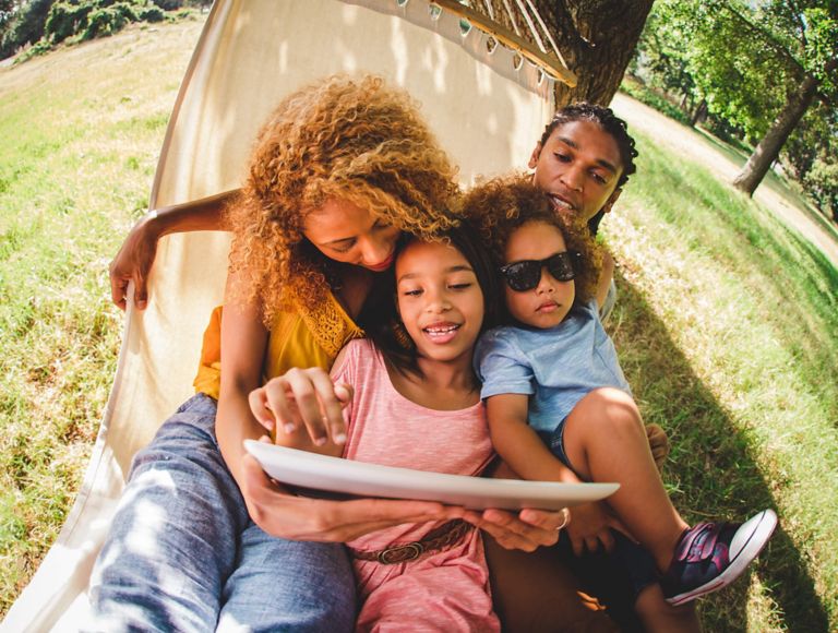 Familia sentada en una hamaca viendo contenidos en una tablet.