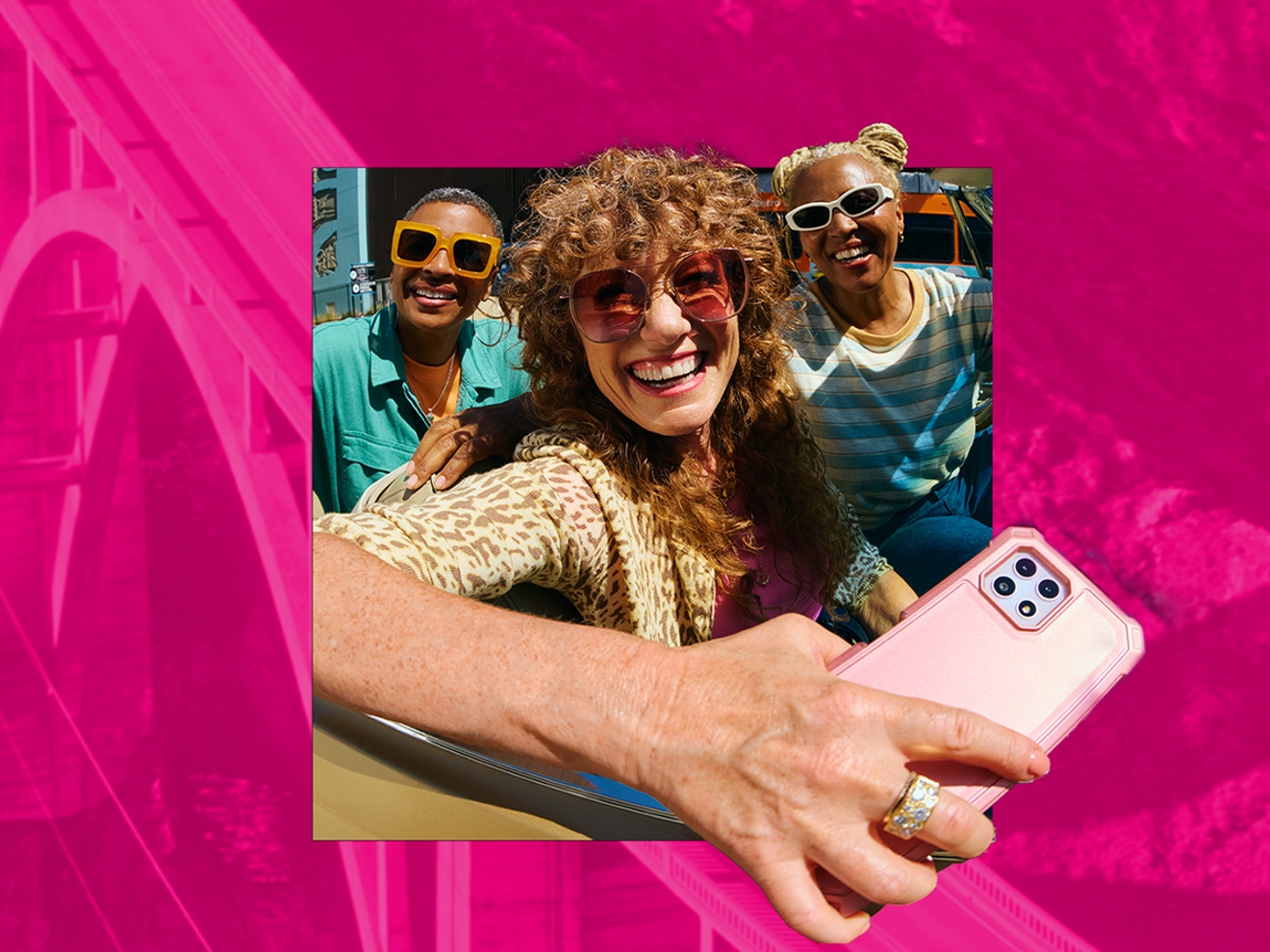 Tres amigos sonriendo con gafas de sol de colores mirando al frente, mientras el amigo del centro sostiene un smartphone blanco con una funda transparente de color rosa.
