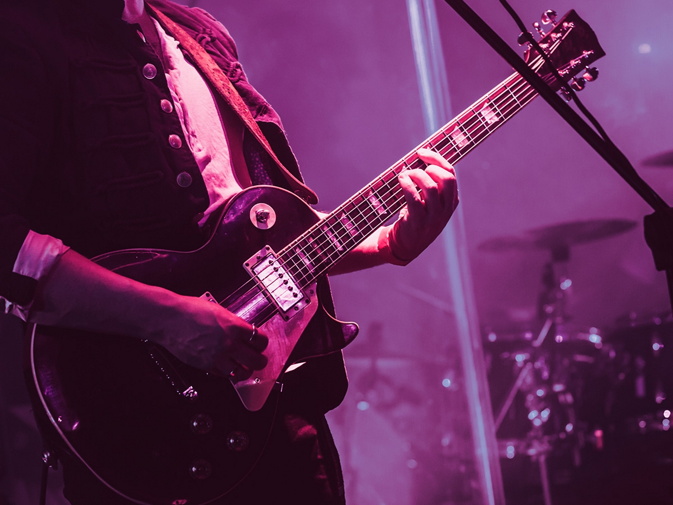 Guitarrista tocando en el escenario con una iluminación magenta.