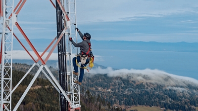 Trabajador de T-Mobile subiendo a una torre de microondas alta con una montaña de fondo