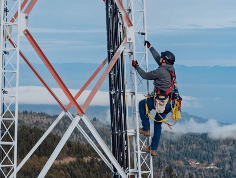 Trabajador de T-Mobile subiendo a una torre de microondas alta con una montaña de fondo