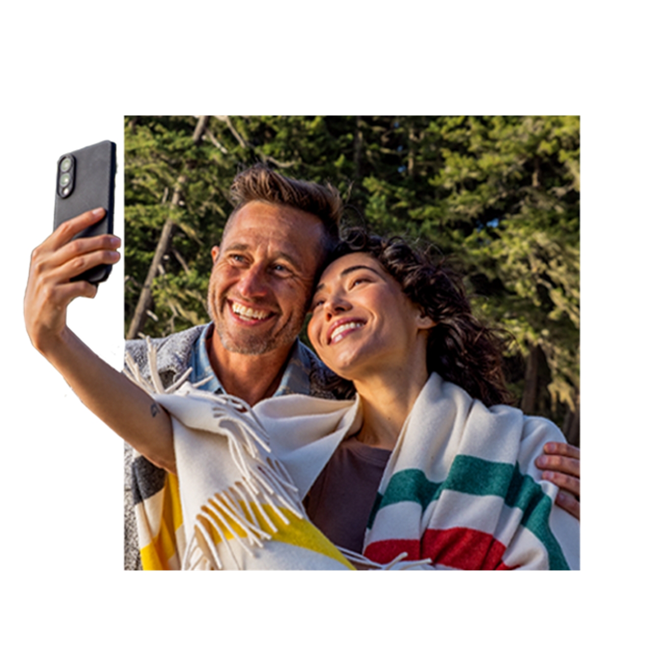 Una mujer envuelta en una manta a rayas sostiene su teléfono mientras sonríe para tomarse un selfie con un hombre.