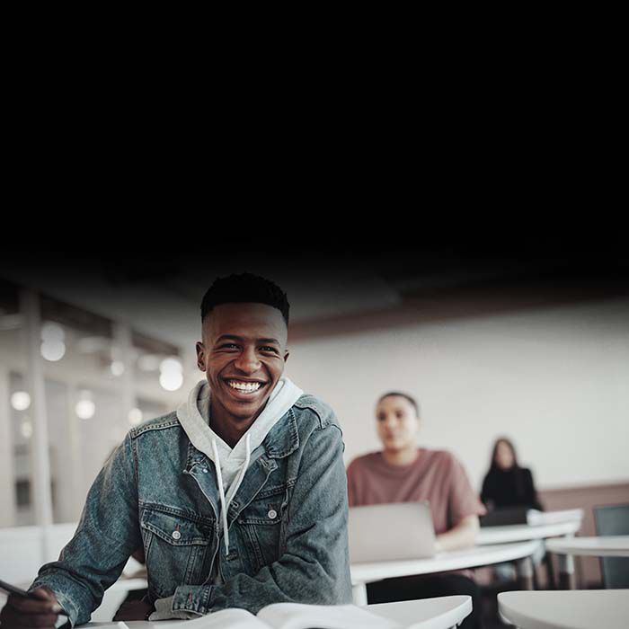 Un estudiante sentado en un escritorio en un aula y sonriendo.