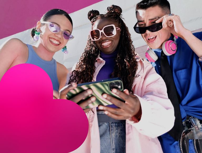 Dos mujeres y un hombre con gafas de sol sonríen mientras miran algo en un teléfono.