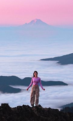 Foto tomada desde lejos de una mujer con una camiseta rosa y una montaña alta nevada al fondo.