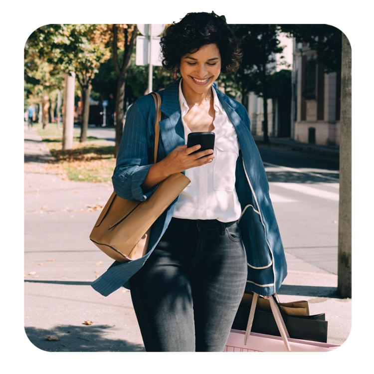 Una mujer camina por la vereda y sonríe a su teléfono.