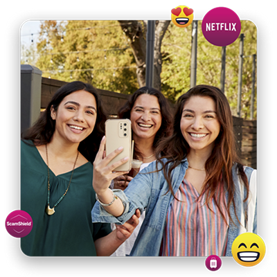 Tres mujeres jóvenes sonriendo. Una sosteniendo un teléfono.