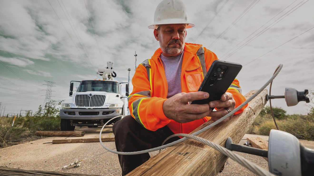 Un trabajador de servicios públicos en una zona rural usa su smartphone para enviarse mensajes con un compañero de equipo.