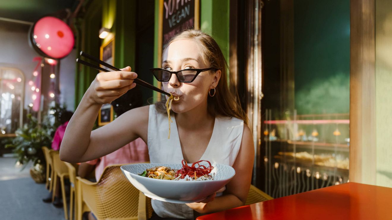Una usuaria de T-Mobile disfruta de un bol de fideos en una cafetería al aire libre.