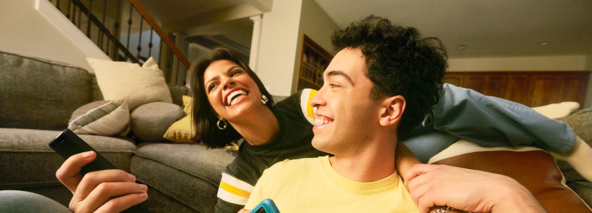 Una pareja bromeando sentada en un sofá con los teléfonos en la mano.