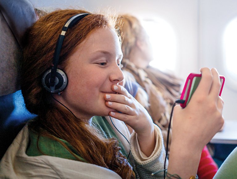 En un avión, una niña usa auriculares y sonríe mirando su teléfono.
