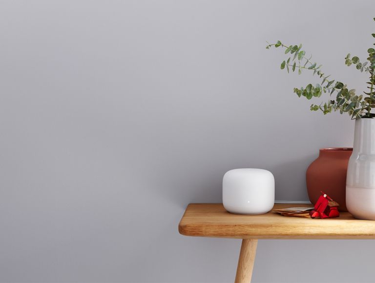 Un Google Nest en una mesa de entrada junto a un gran jarrón con plantas.