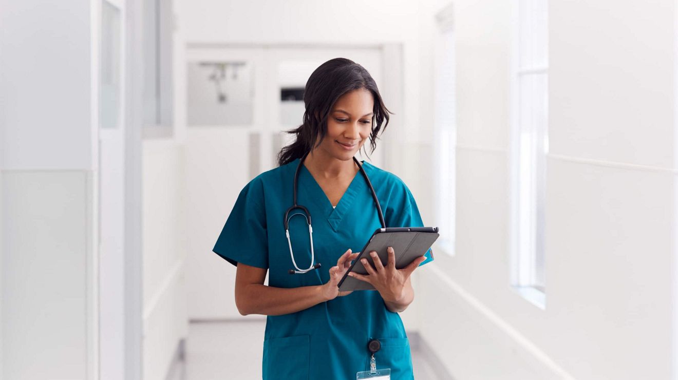 Enfermera revisando datos de pacientes en una tablet conectada de T-Mobile mientras camina por el pasillo de una clínica.