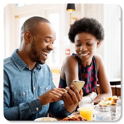 Una pareja en un restaurante sonríe a su teléfono.