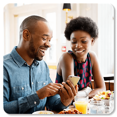 Una pareja riendo mientras mira un teléfono y cena.