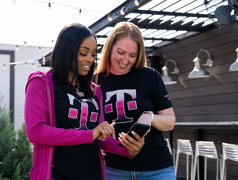 Dos personas al aire libre luciendo camisetas de T-Mobile mirando el teléfono de una de ellas