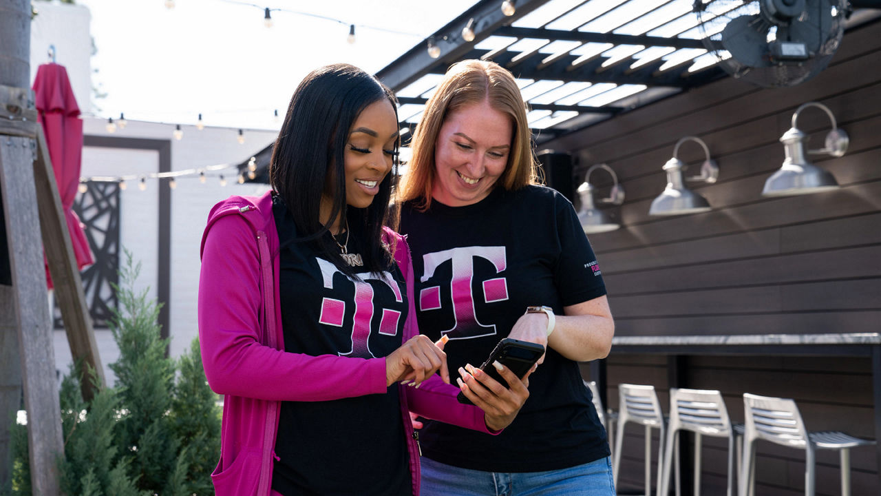 Dos empleados de T-Mobile sonrientes miran un teléfono inteligente