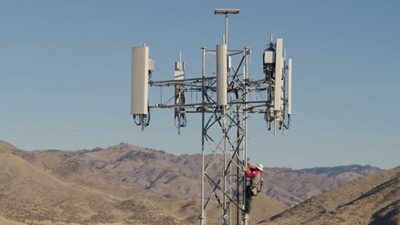 Técnico de T-Mobile subiendo a una torre celular con montañas en el fondo