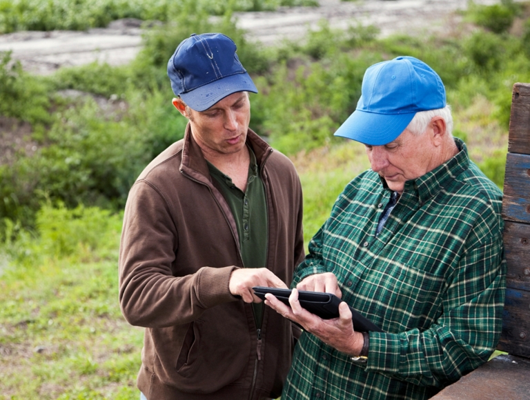 Dos granjeros trabajando en una tablet cerca de una plataforma de un camión