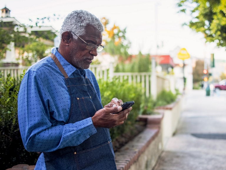 Trabajador de un taller usando un smartphone en la acera de la ciudad